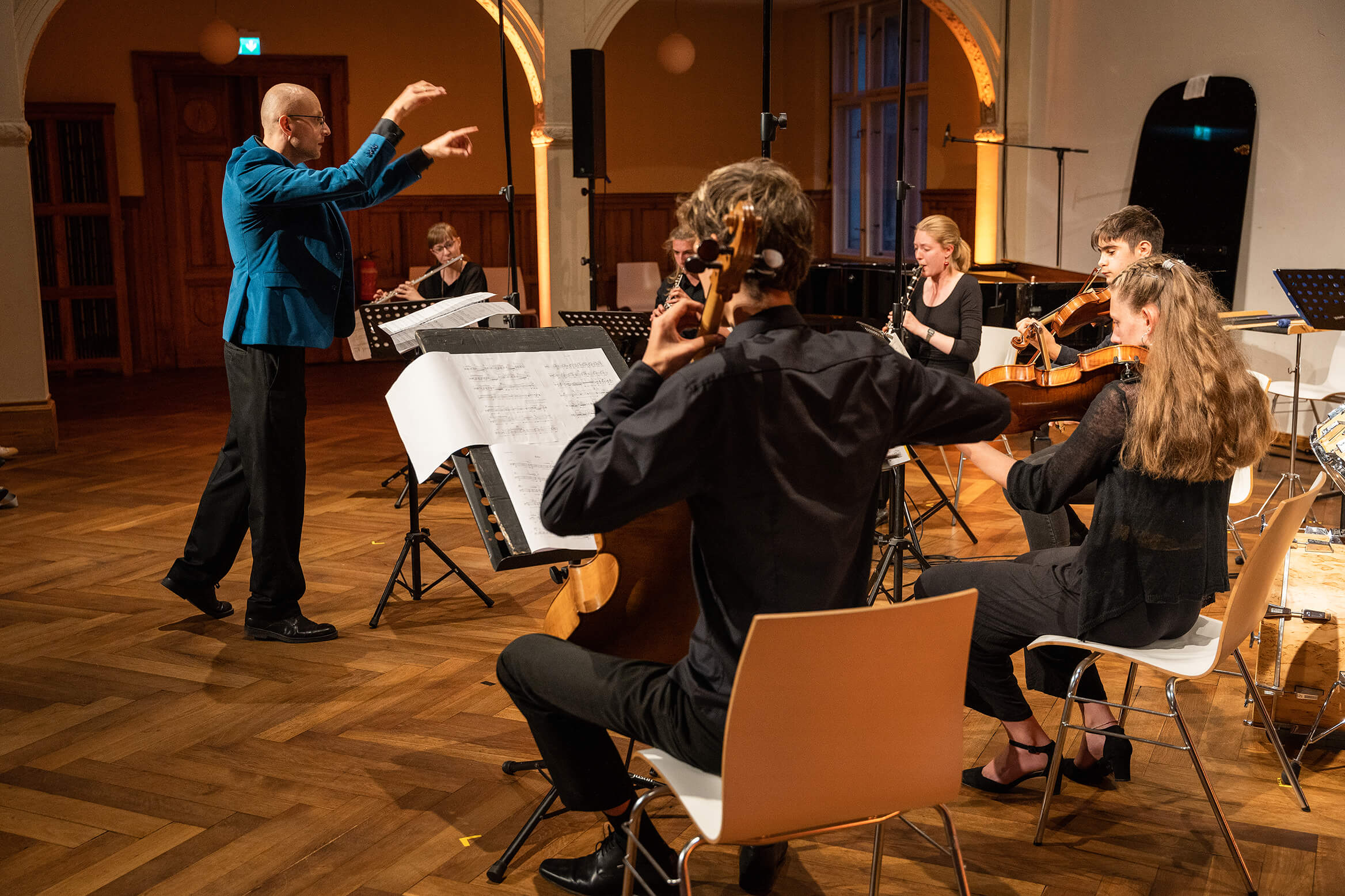 Das Bild zeigt einen Dirigent und das Orchester, welches er anleitet, beim spielen.