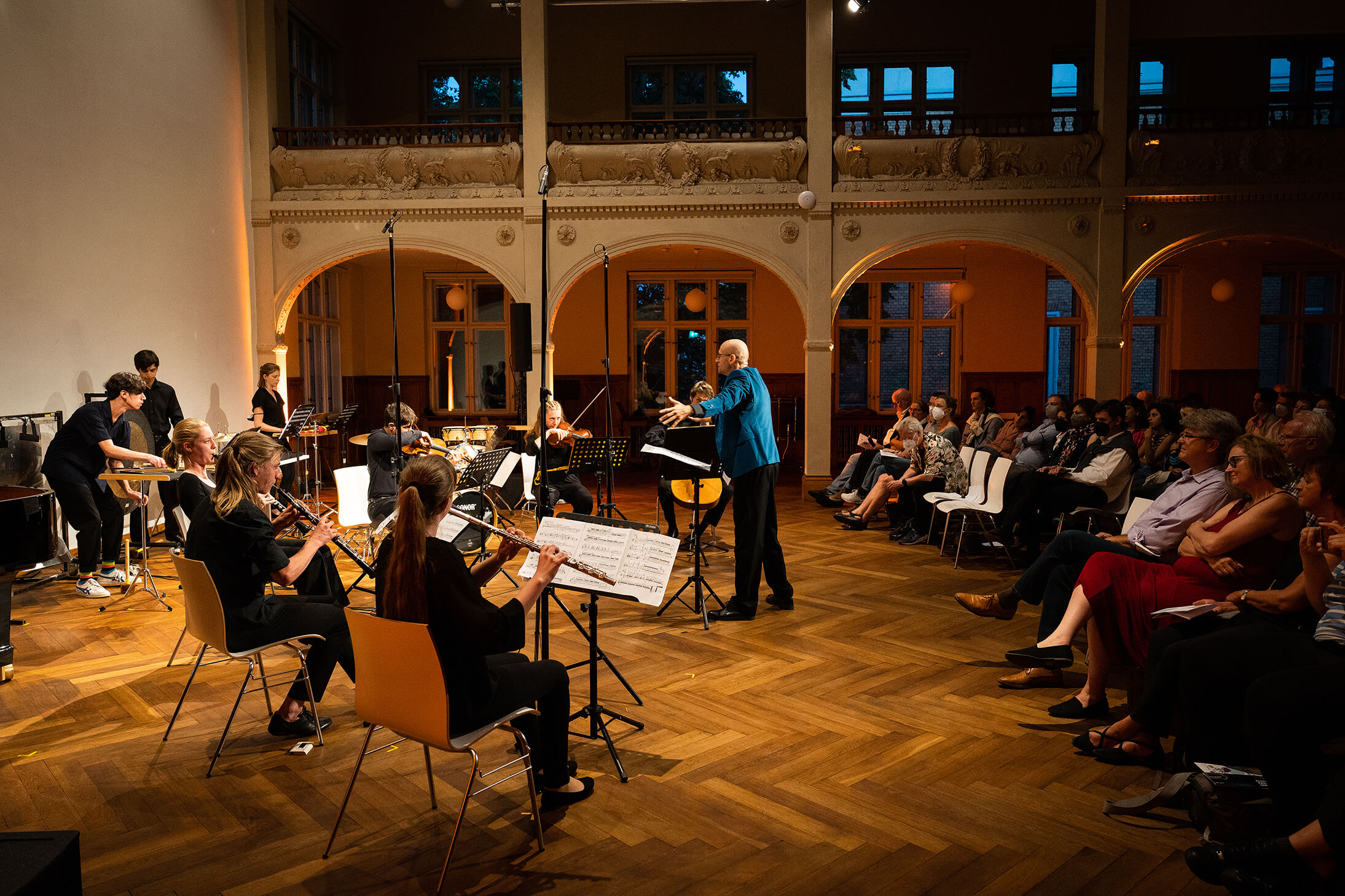 Das Bild zeigt in einer totale das junge Orchester und den Dirigenten im Konzertsaal. Auch die gebannten Zuschauer:innen sind zu sehen.